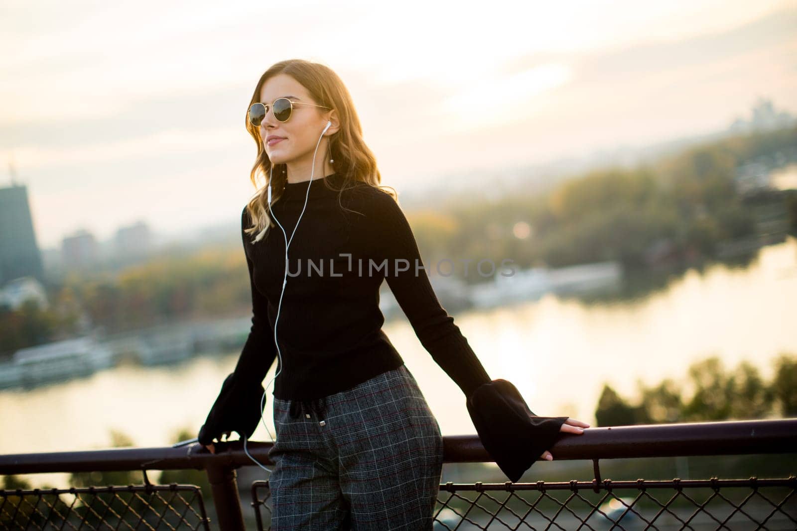 Portrait of trendy young woman listening music from smartphone outdoor at sunset