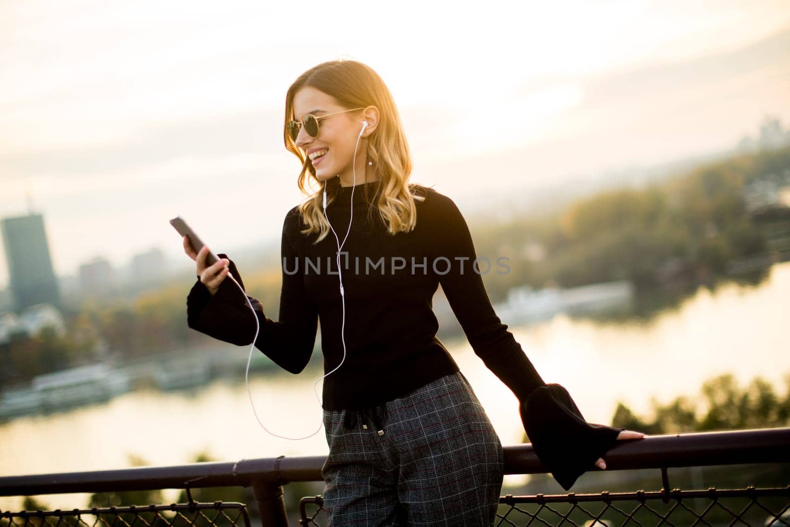 Trendy young woman listening music from smartphone outdoor at sunset