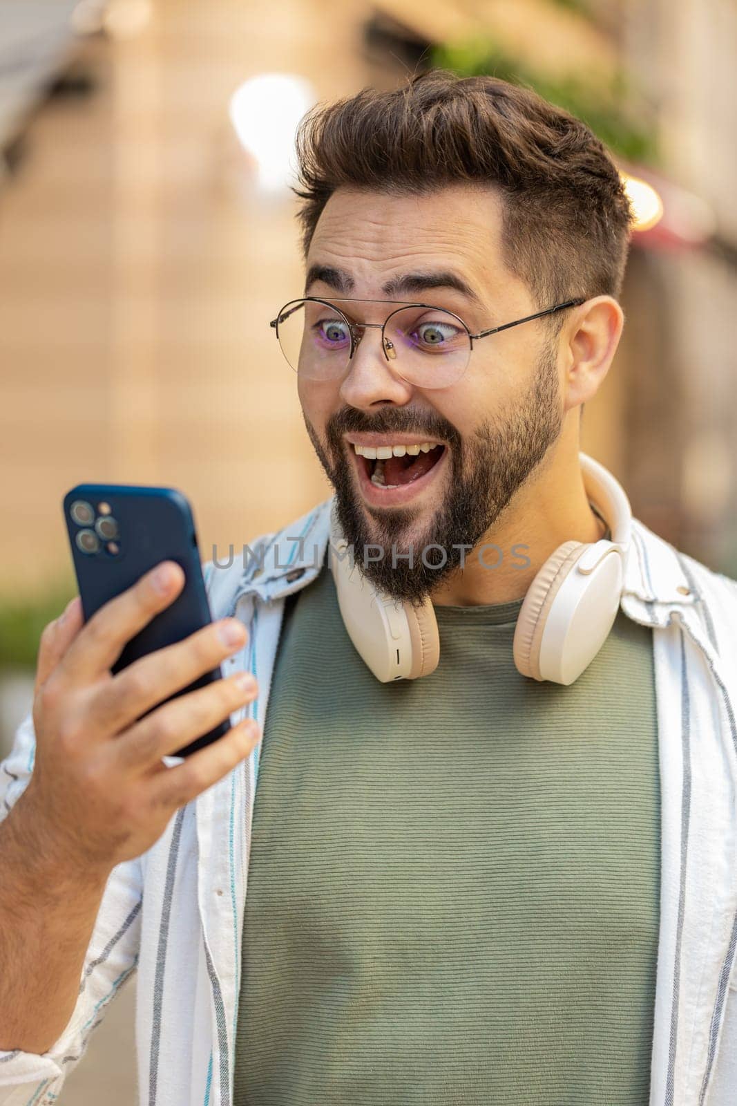 Excited amazed Caucasian man outside using mobile phone device winning online shocked male tourist in city win smartphone bet celebrate victory achievement success. Guy standing on urban city street.