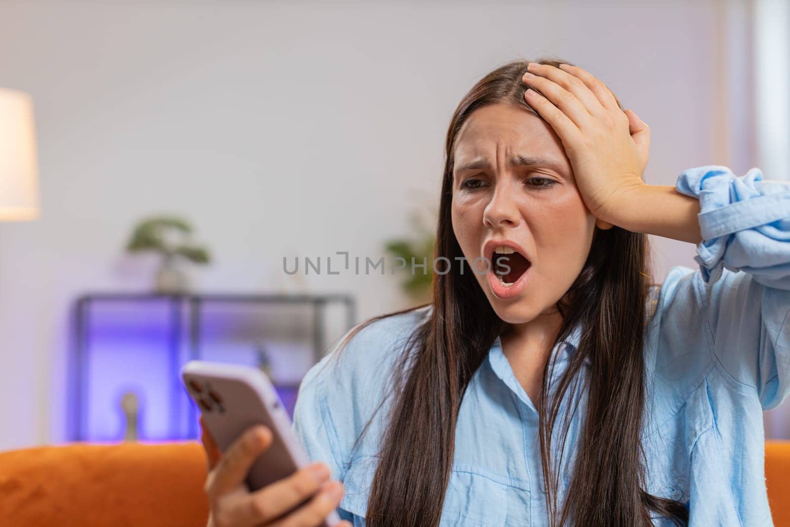 Sad displeased Caucasian woman using smartphone typing browsing, loses becoming surprised sudden lottery game results, bad news, fortune loss fail, deadline, virus. Young girl at home room on couch