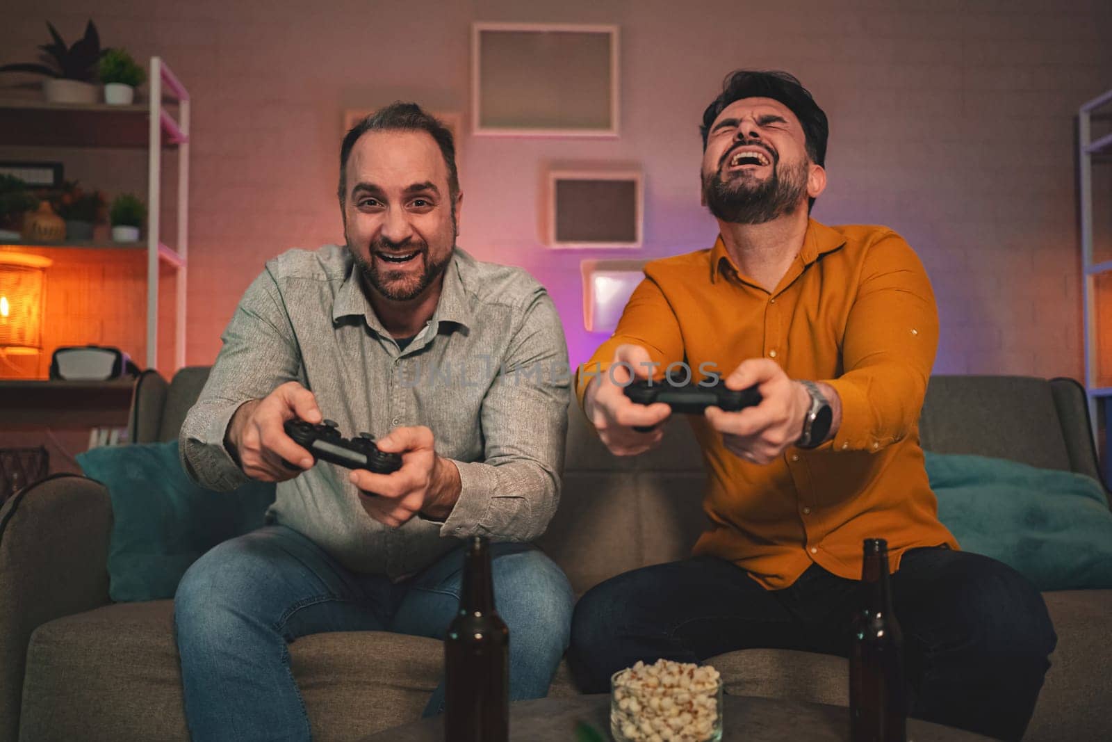 In a comfortable and inviting living room, two friends are deeply engaged in a thrilling gaming session. With joy on their faces, they hold controllers tightly, surrounded by snacks and drinks.