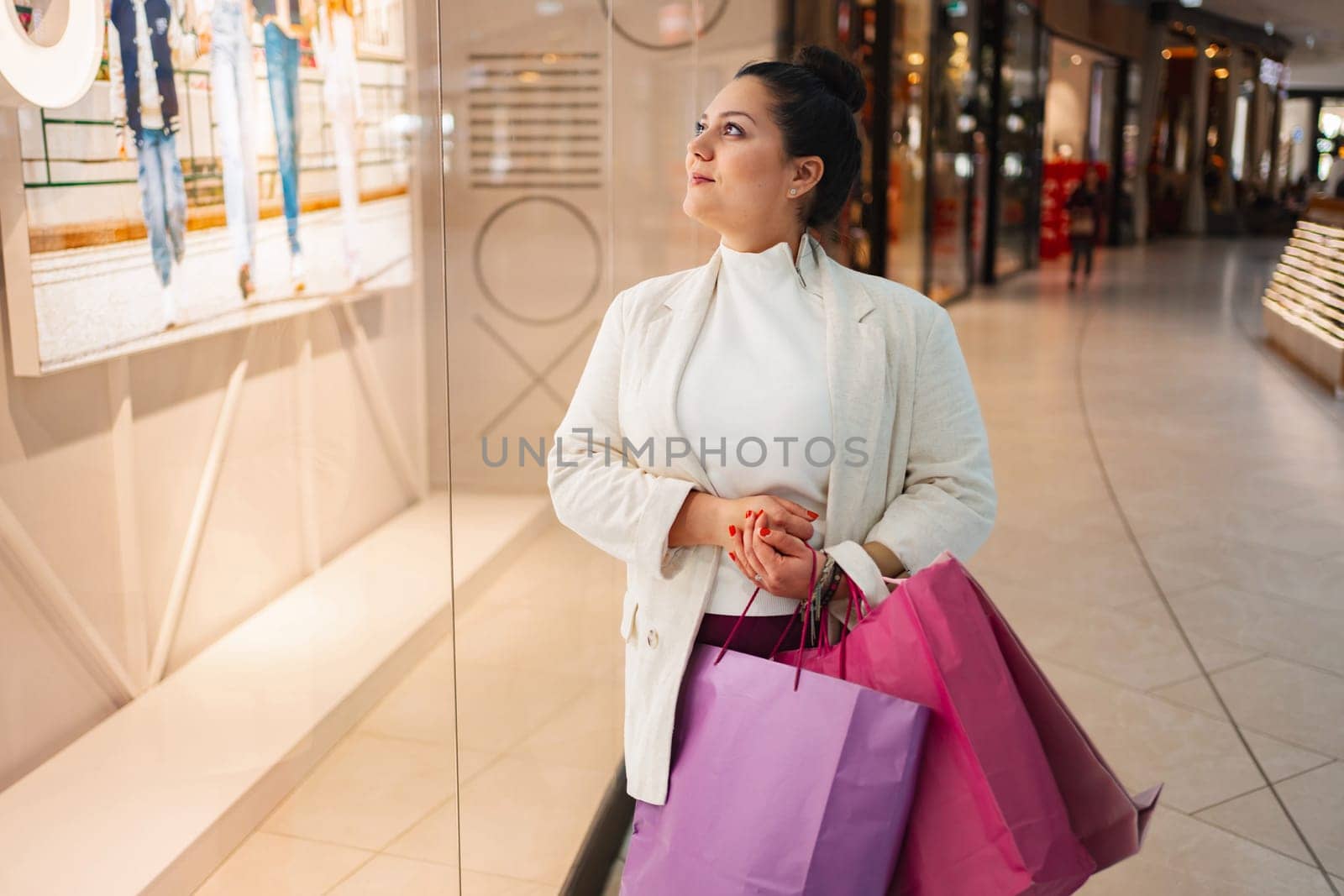A woman admires window displays while holding colorful shopping bags.