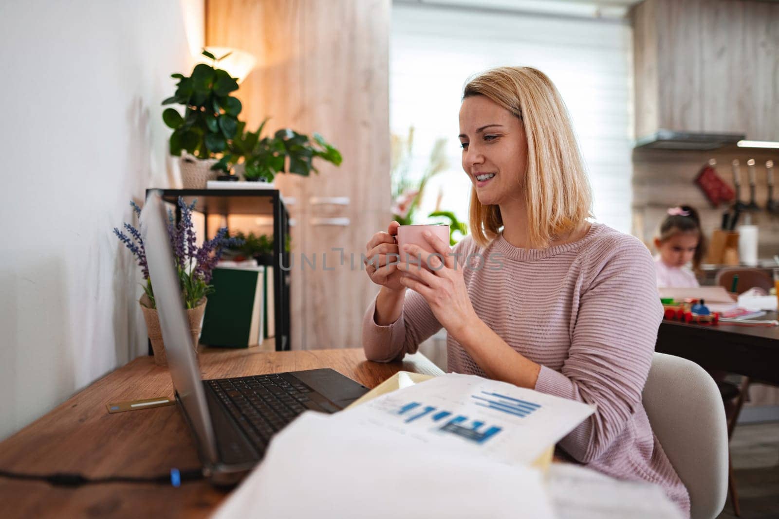 Person focuses on a laptop screen while sipping coffee, relaxing at home.