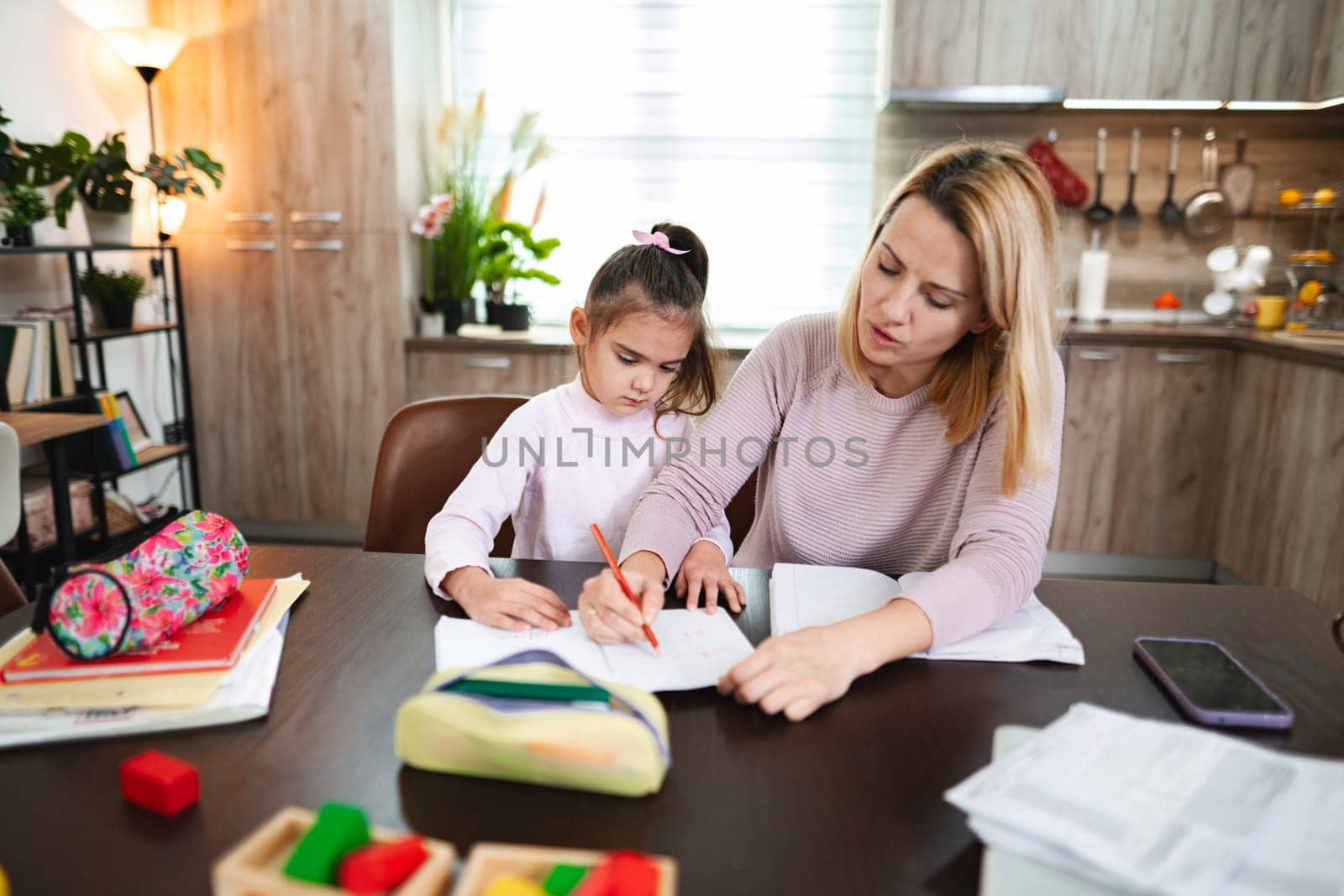A mother assists her daughter with homework at a cozy kitchen table.