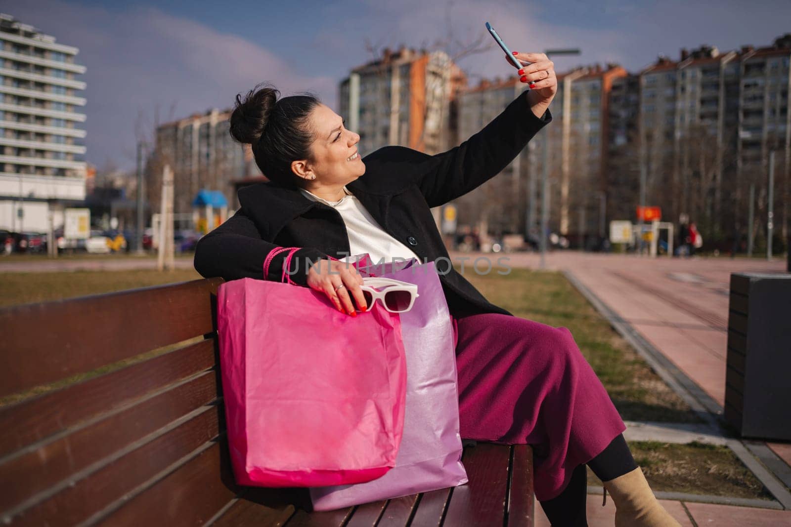 A woman enjoys her shopping haul while taking a selfie outdoors.