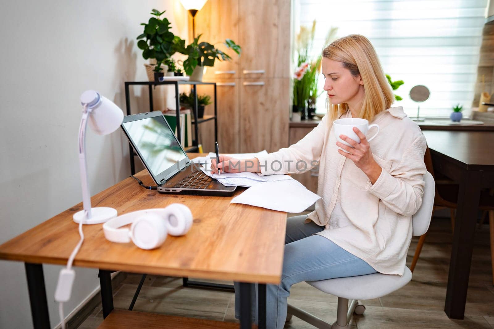 Woman enjoying tea while working on a laptop in a bright room.