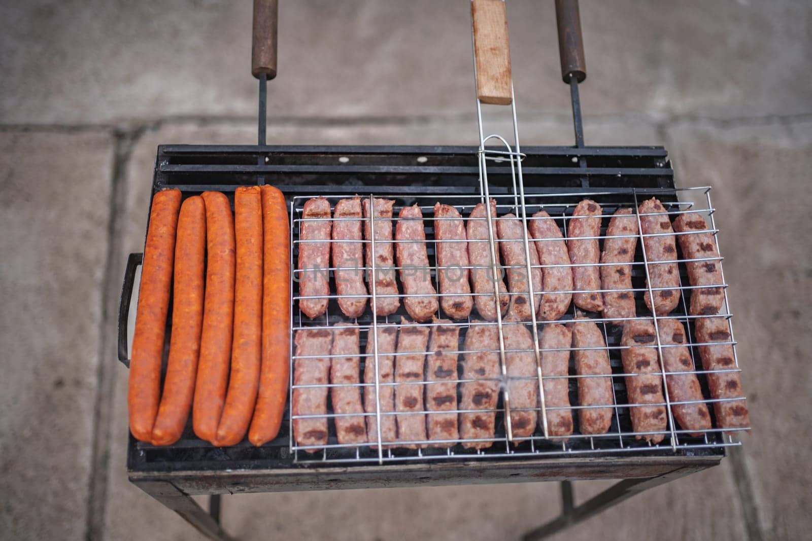 Juicy sausages and bright hot dogs cook over an open flame outdoors.