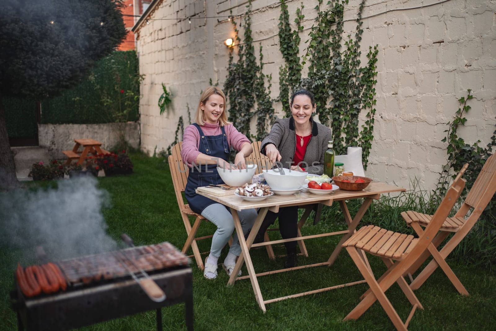 Two friends prepare food together outdoors on a sunny day.