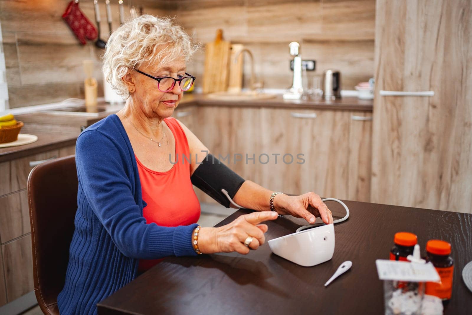 A senior woman checks her blood pressure while seated in her stylish kitchen.