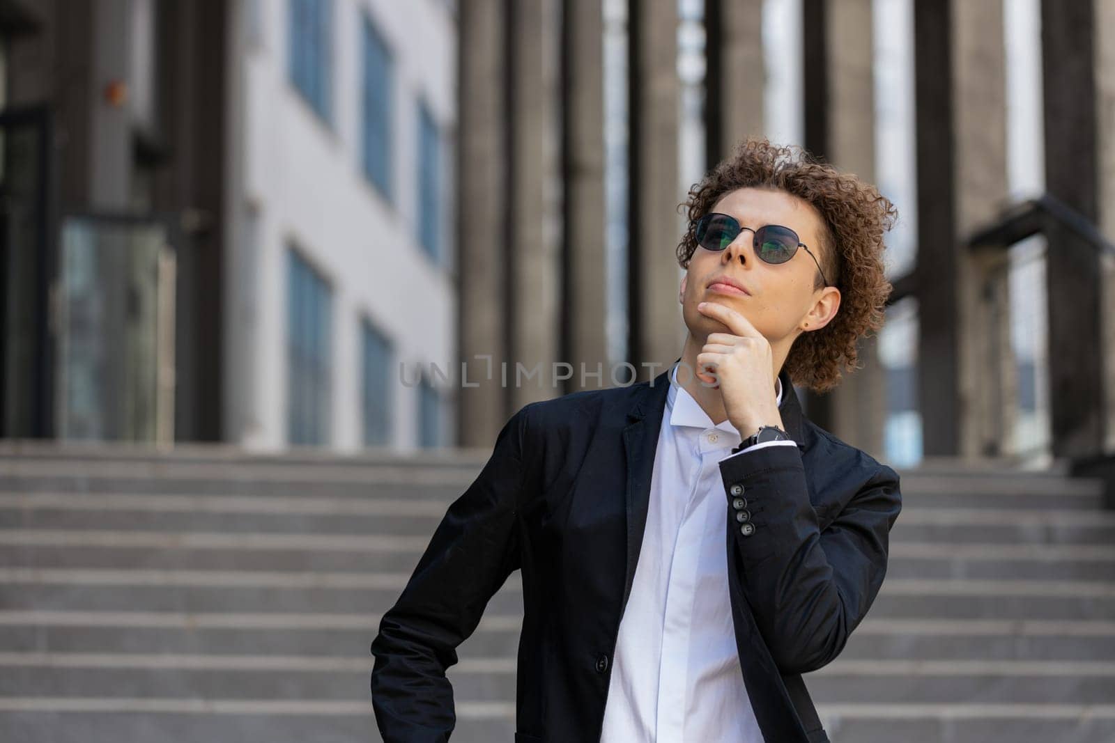 Portrait of Caucasian puzzled businessman professional standing outdoors deep in thoughts thinking recollecting memory creating plan. Handsome man in formalwear and sunglasses on downtown city street.
