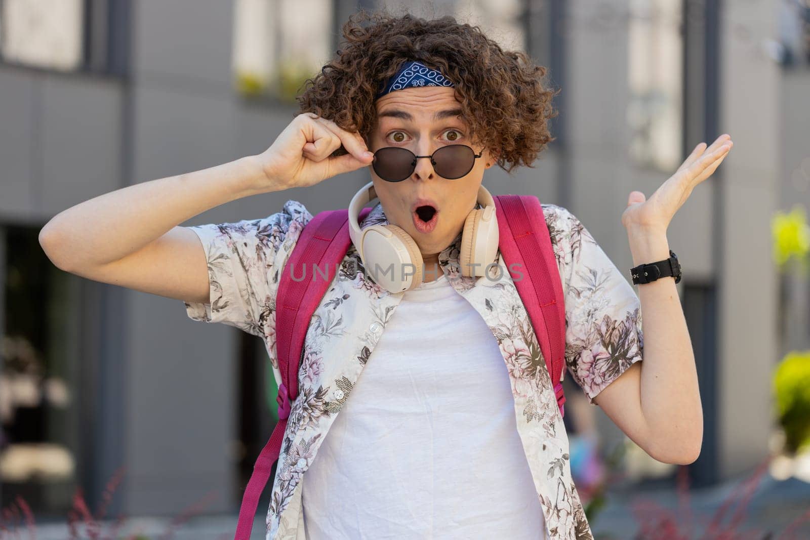 Oh my God, Wow. Happy young man taking off sunglasses looking surprised at camera with big open eyes, shocked by sudden victory, game winning, lottery goal achievement, good news outdoors city street.