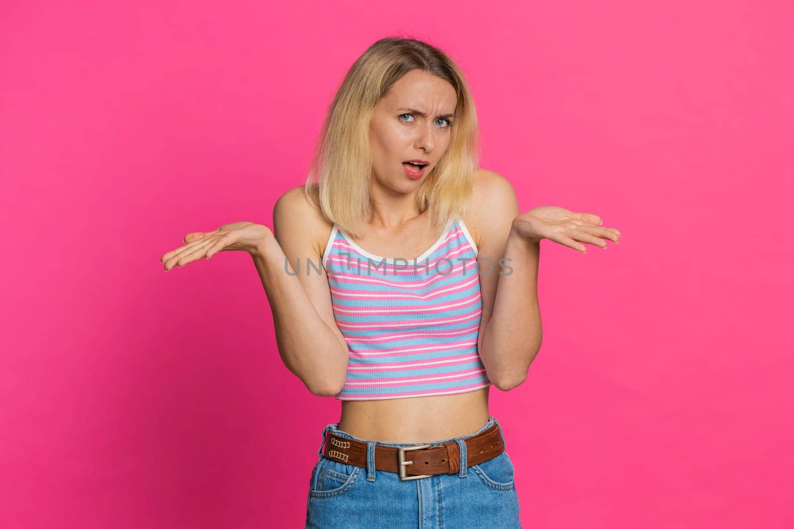 What. Why. Angry confused young woman in crop top raising hands in indignant expression, asking reason of failure, demonstrating disbelief irritation by troubles. Girl isolated on pink background