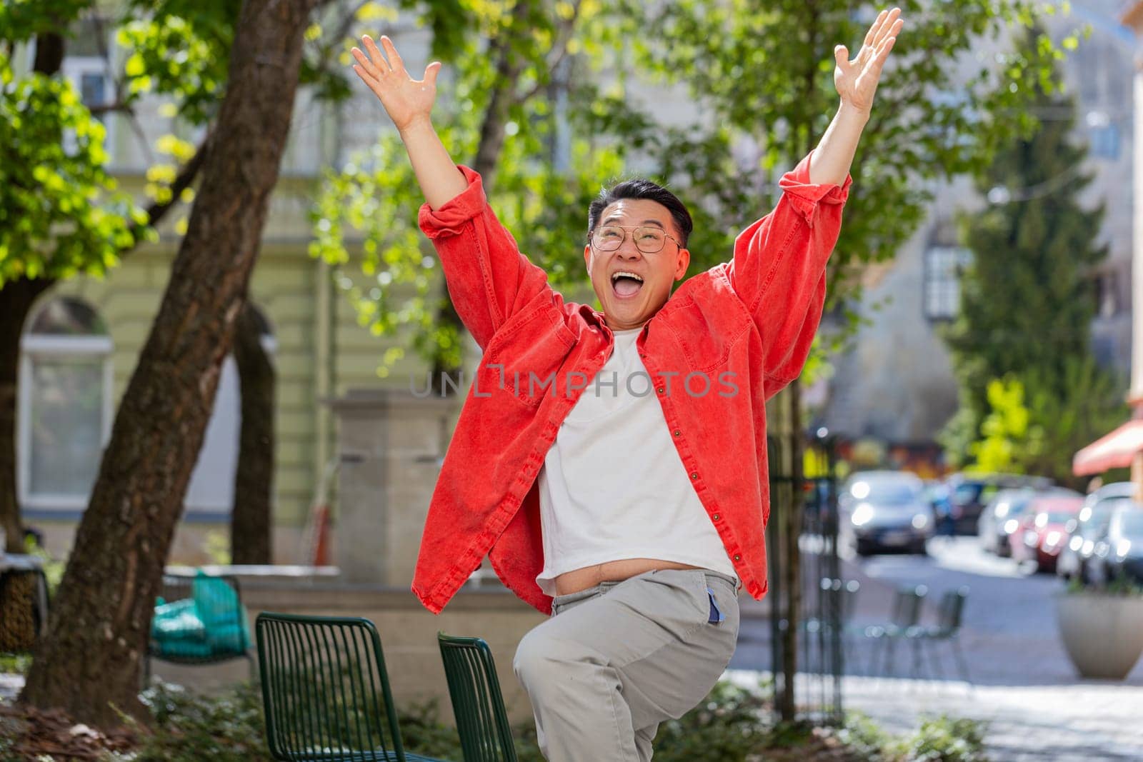 Asian middle-aged man shouting celebrating success winning goal achievement good news lottery jackpot casino luck victory career outdoors. Chinese guy on urban city street. Town lifestyles. Horizontal