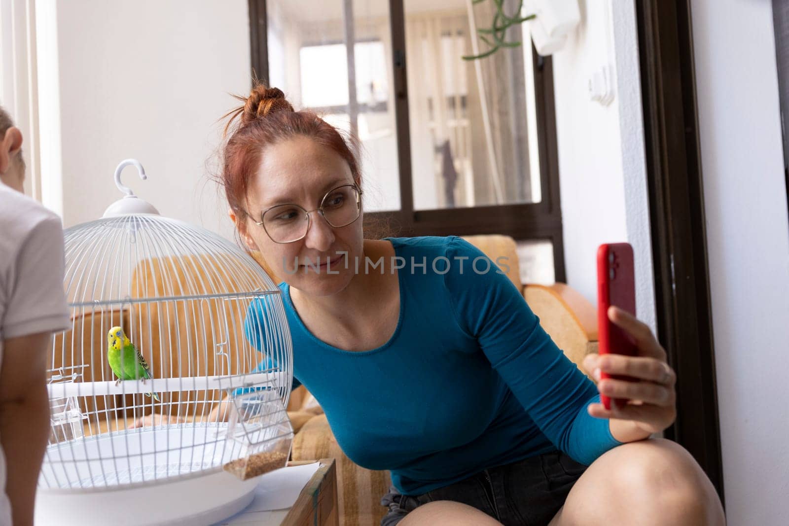 Woman taking pictures of a parrot in a cage with a smartphone, sharing moments with pets