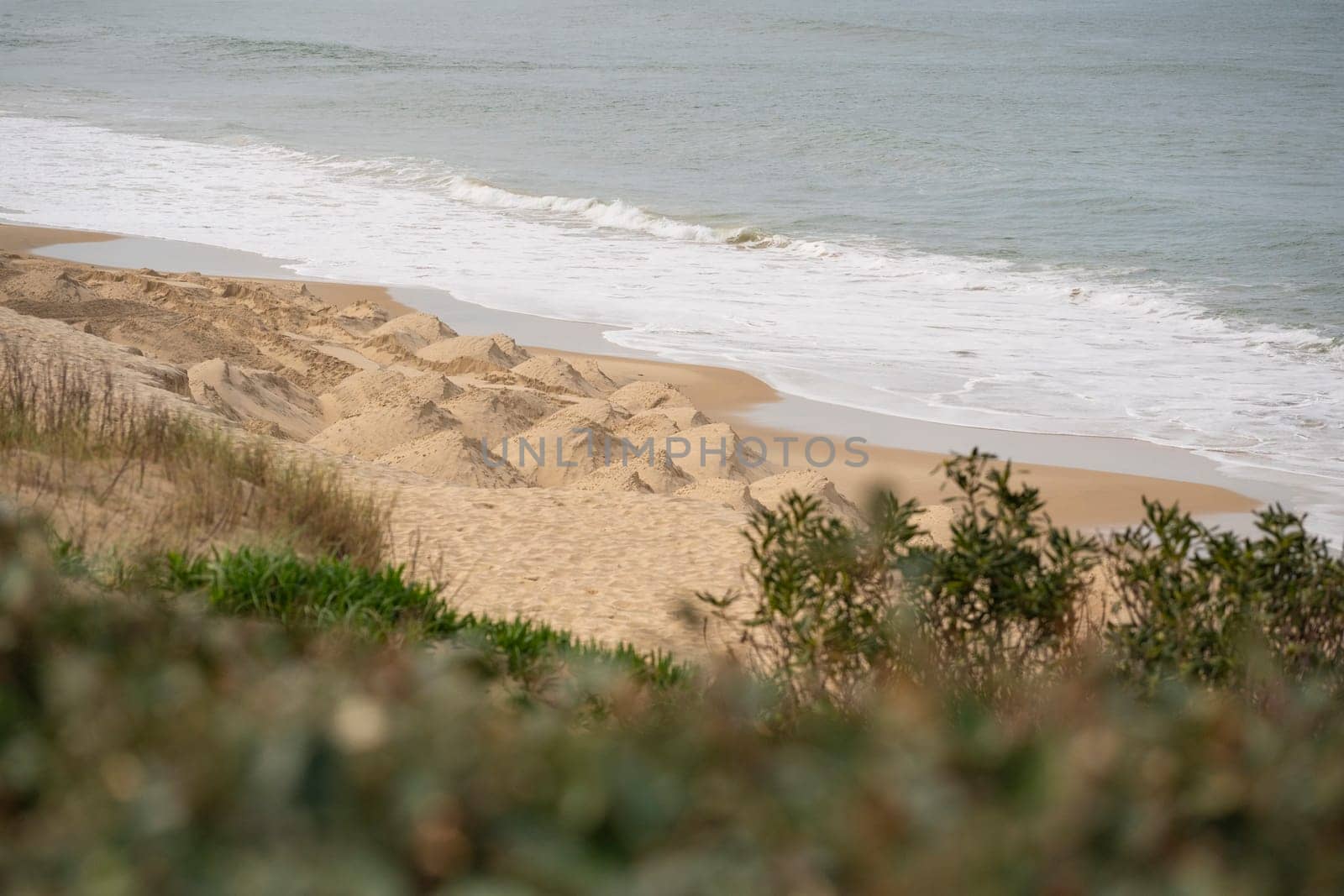 Waves gently lap at the sandy beach of Biscarrosse while soft dunes rise in the background, creating a serene coastal environment on a calm day.