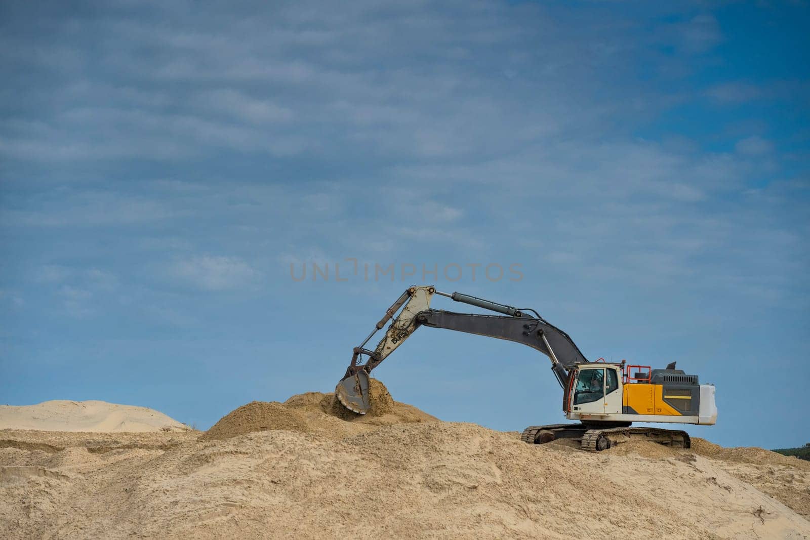 Heavy machinery is actively moving sand along the coastline under a clear blue sky, focusing on erosion control efforts during daylight hours in a coastal area.