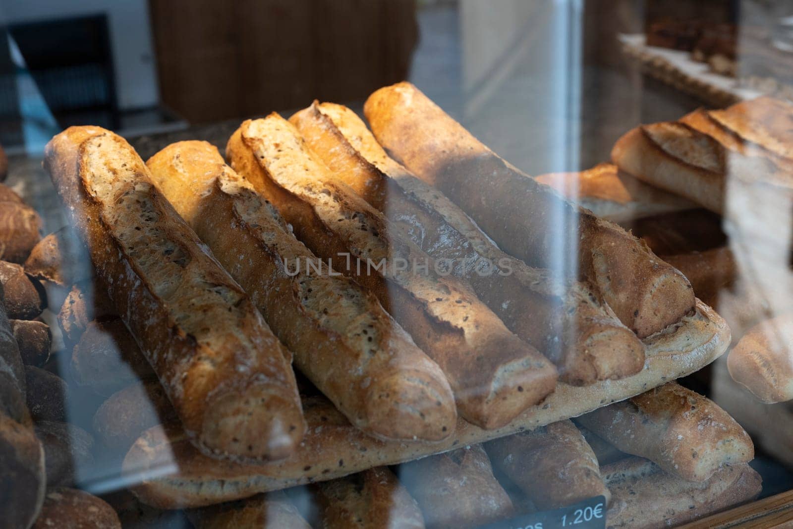 A selection of golden-brown French bread loaves is arranged on a wooden shelf inside a cozy bakery, with natural light casting soft shadows over the crusts.