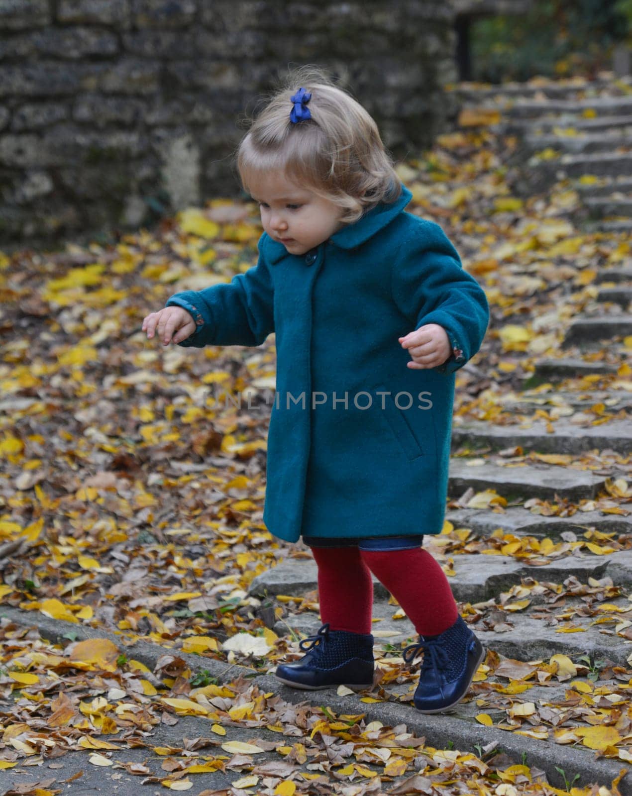 Little girl in the park comes down the stairs with yellow leaves