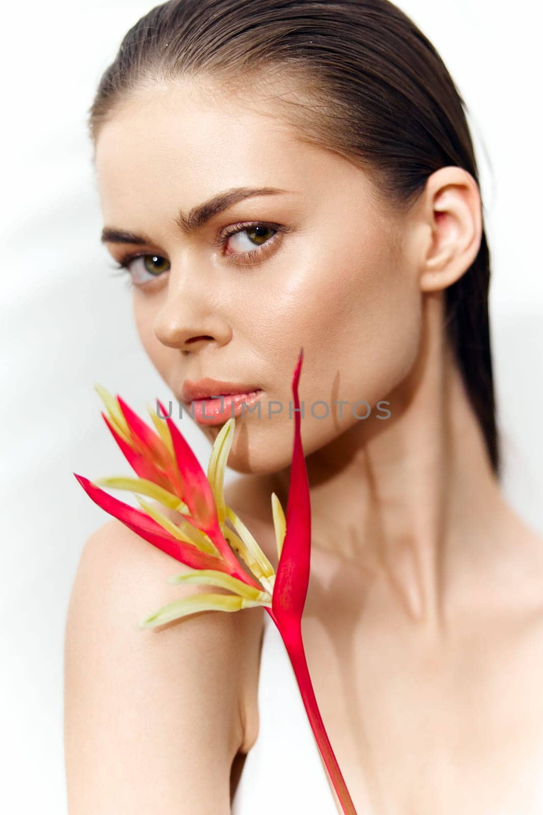 A stunning portrait of a young woman holding a vivid flower, expressing confidence and allure. The minimalist white background enhances her radiant features.