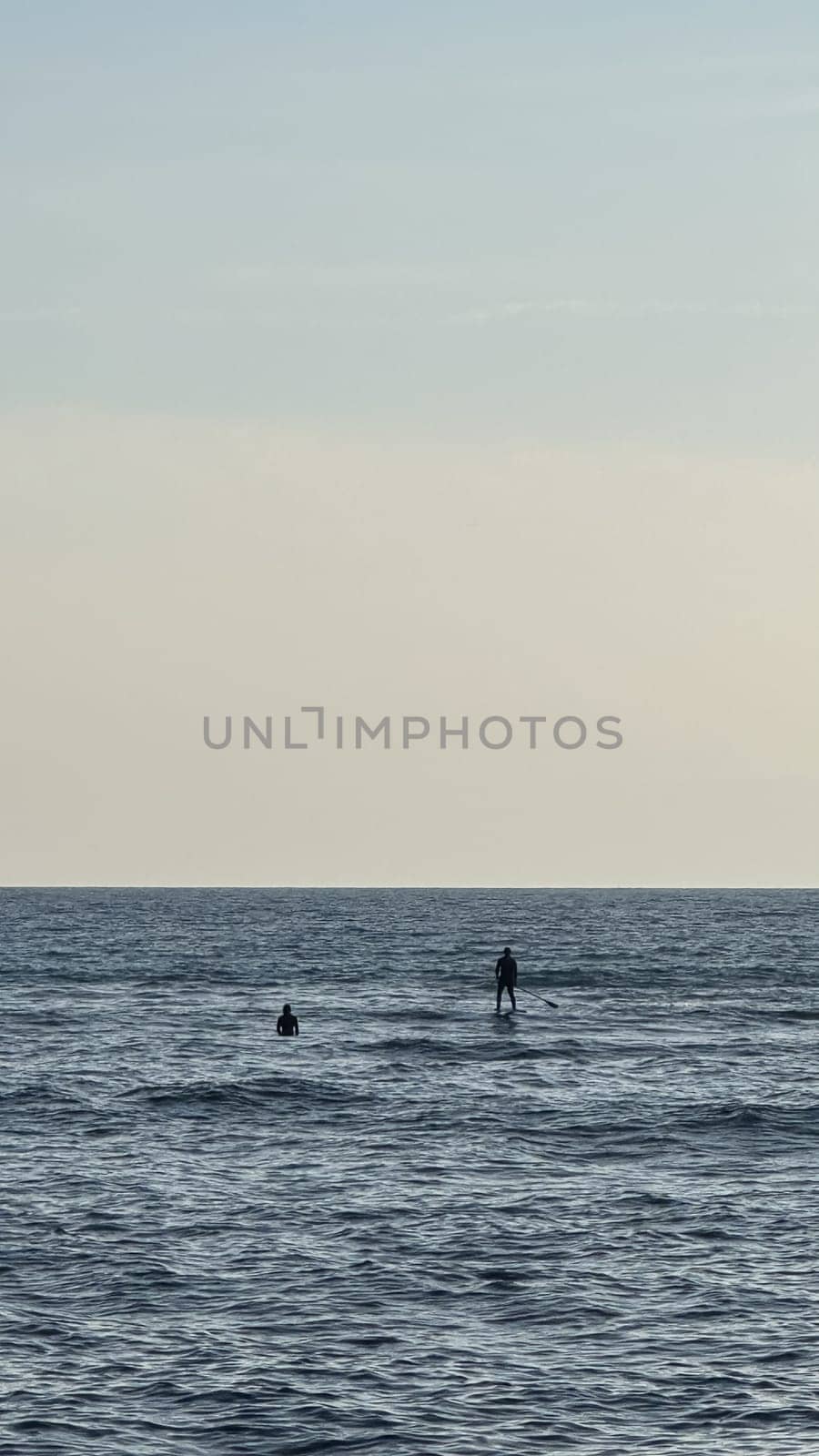 Silhouette of two people on a board with an oar in calm open water under a bright blue sky with fluffy clouds. High quality photos