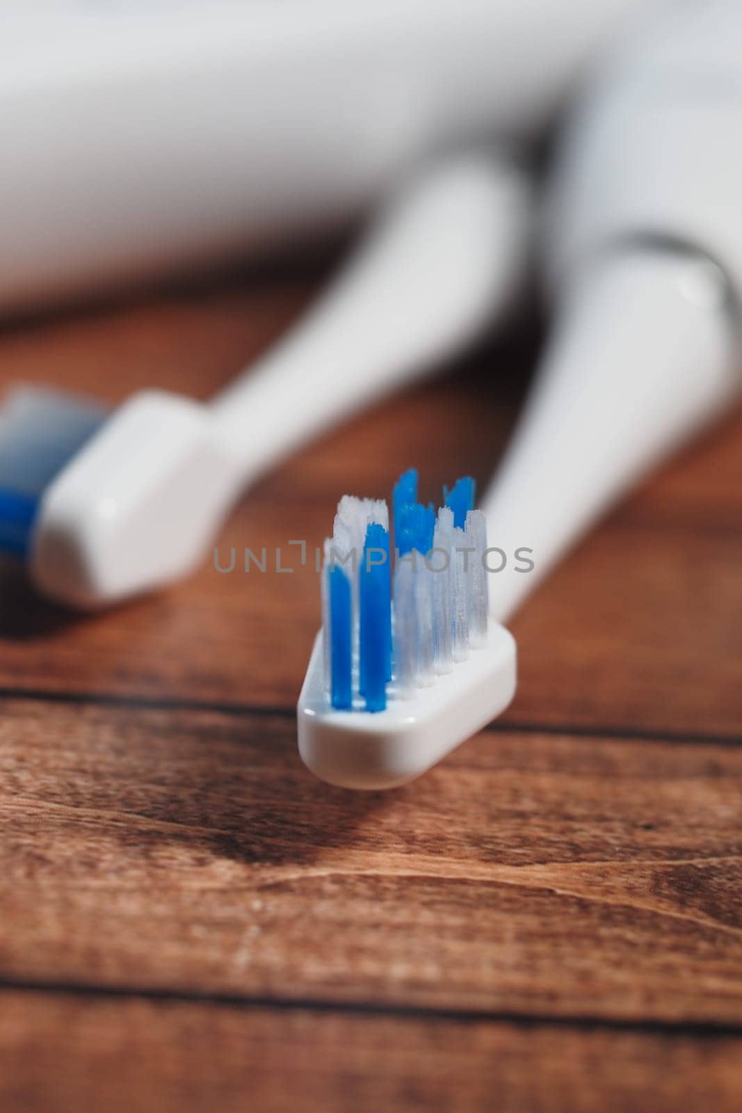 Two electric toothbrushes with blue bristles sit on a wooden surface.
