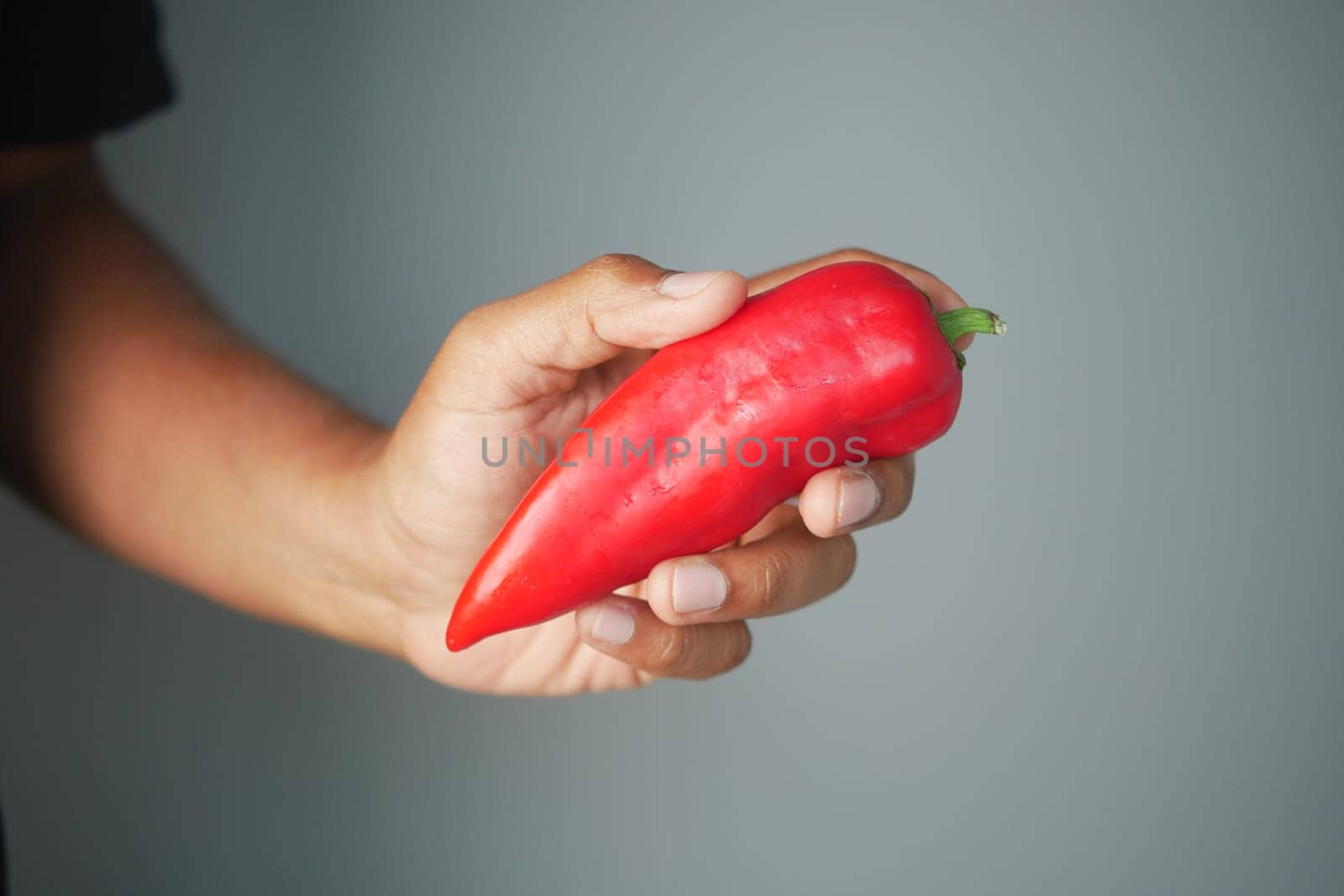 A person is holding a fresh red chili pepper with one hand.