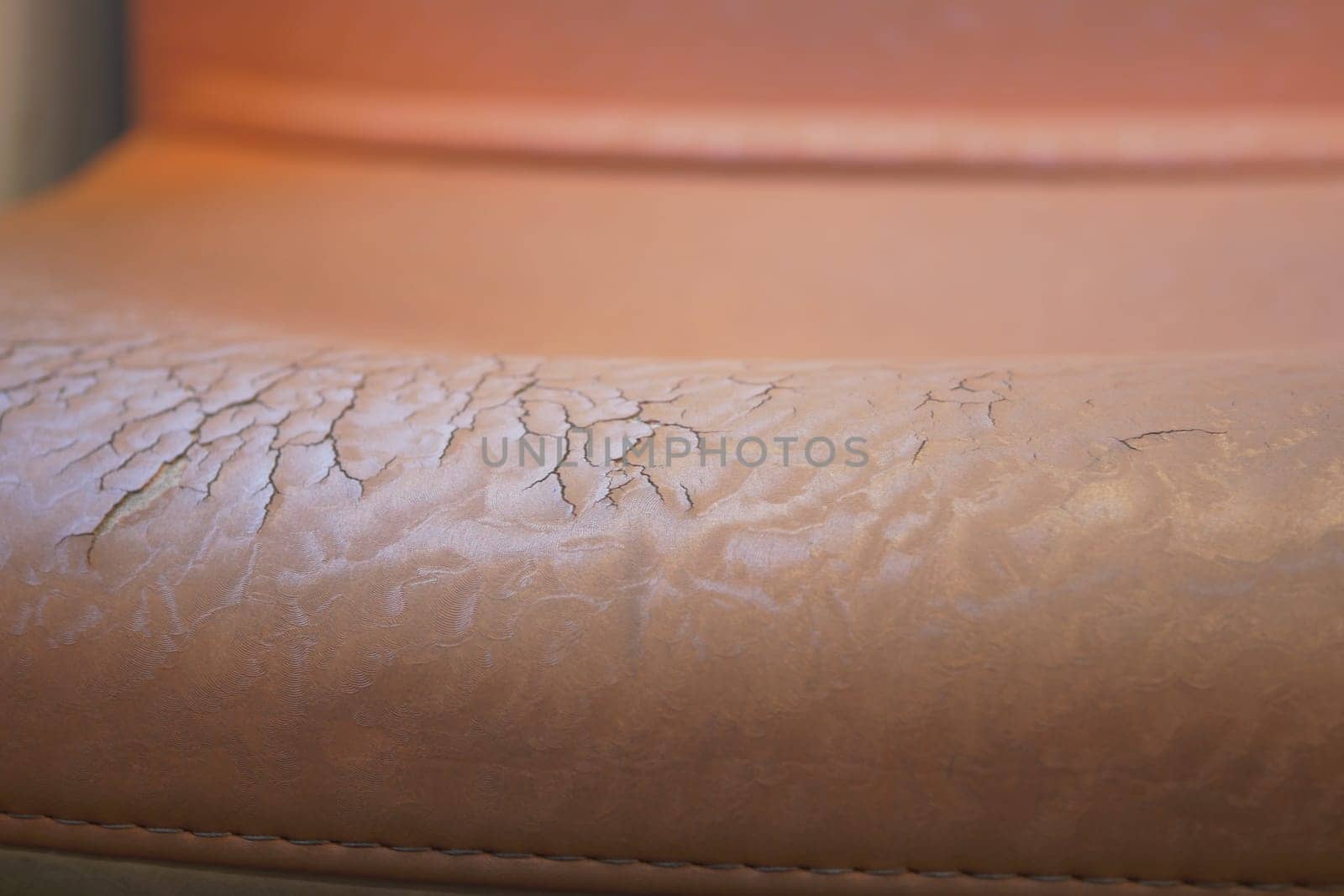 Close-up view of worn leather upholstery on a chair reveals cracks.