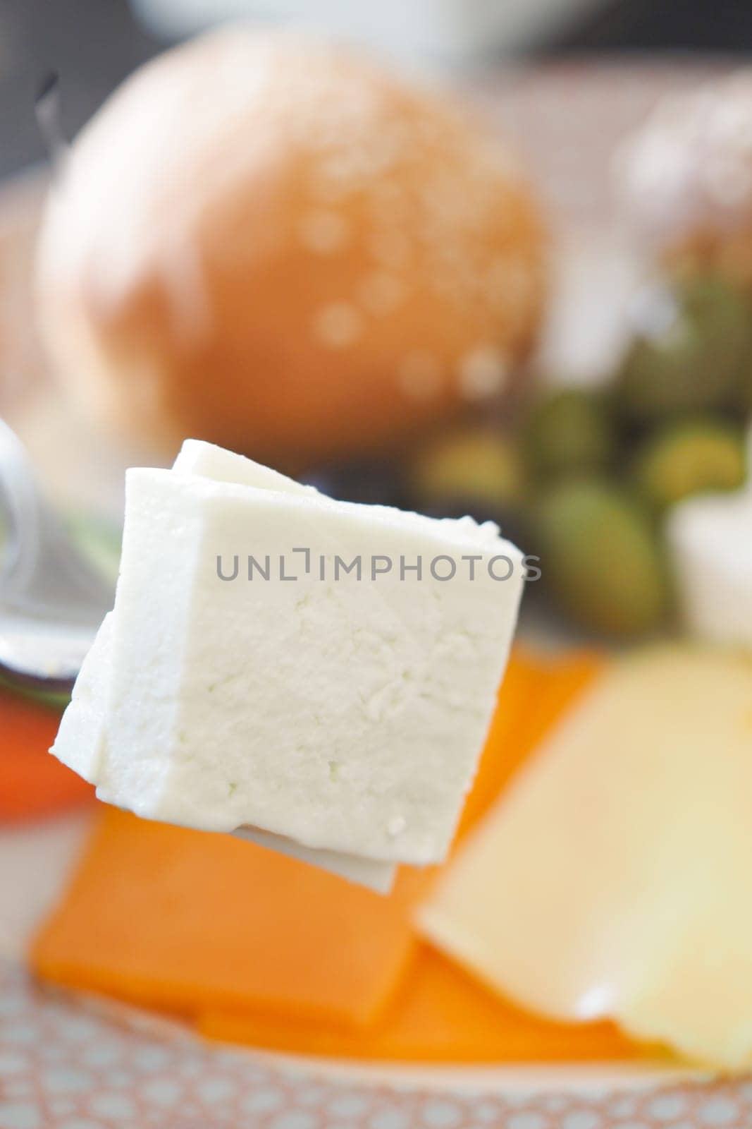 A fork is lifting a cube of cheese above a variety of snacks on a table.
