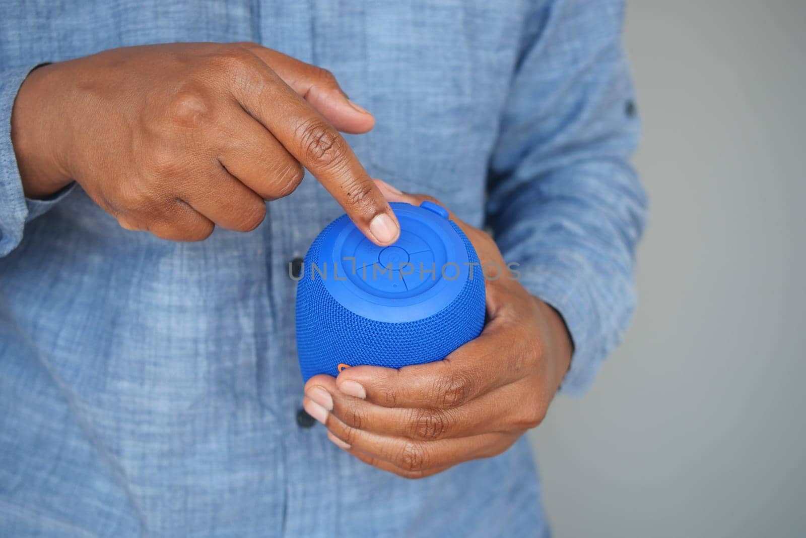 Individual operates a blue wireless speaker while dressed casually.