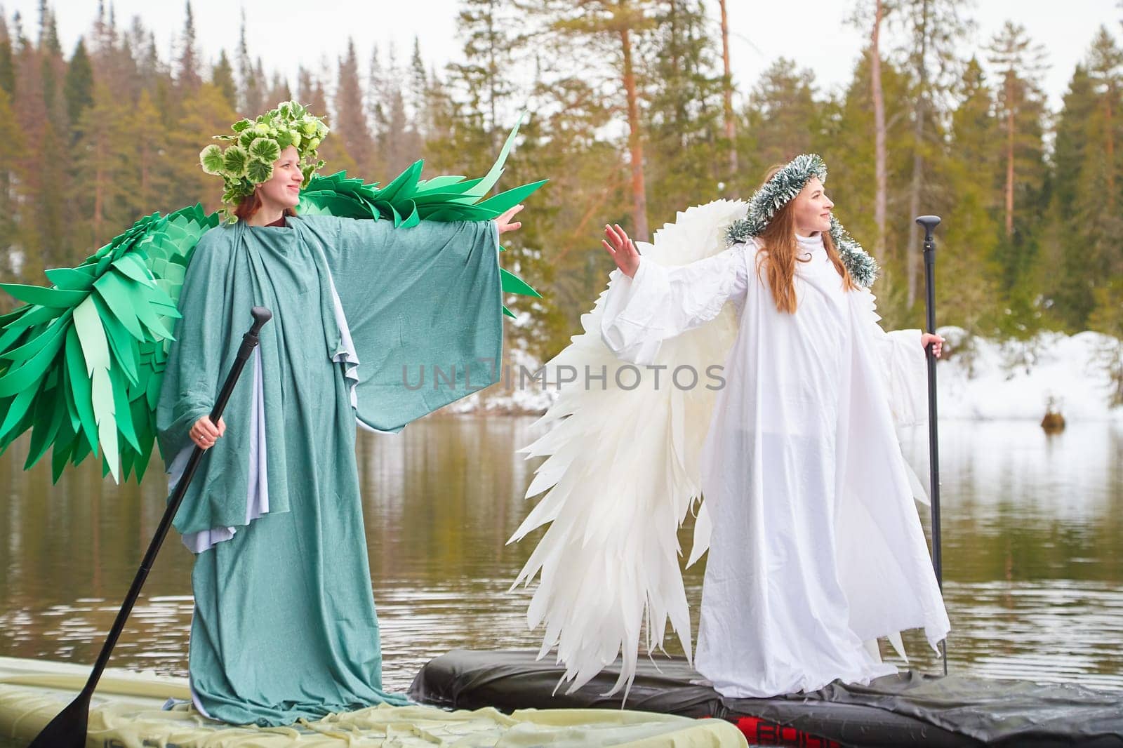 Two girls dressed in white and green dresses stand on a serene lake, embodying the harmonious meeting of winter and spring in a magical moment.