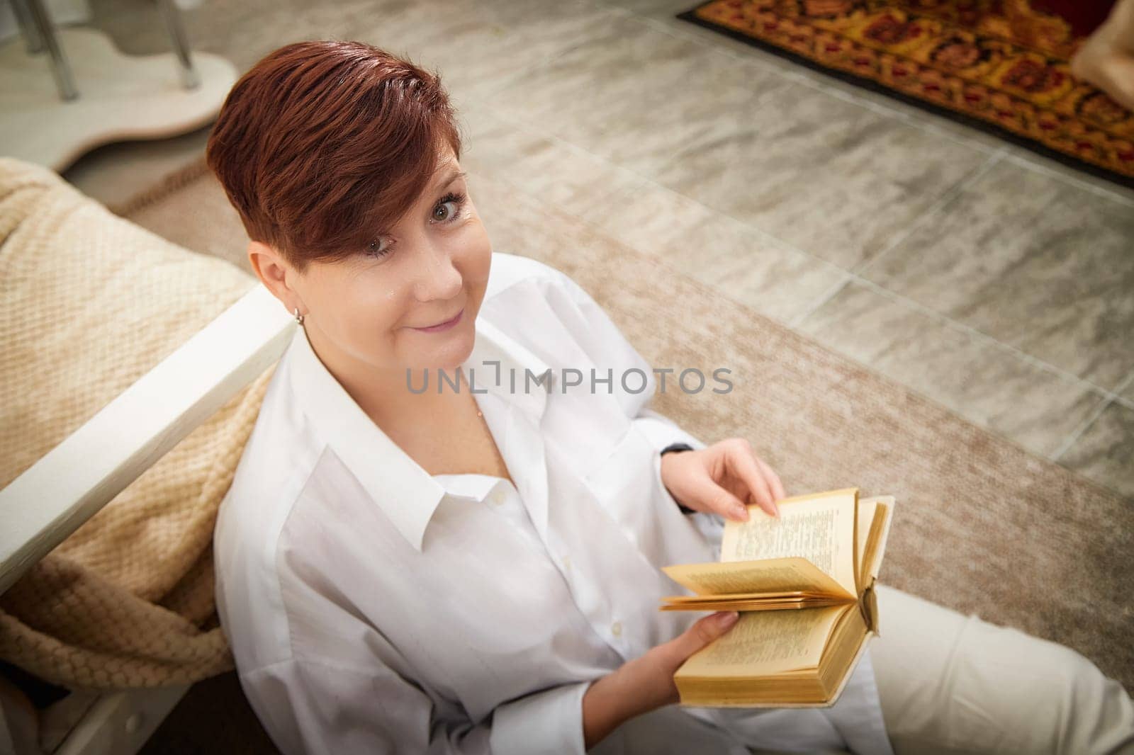 Woman with short hair reads a book while sitting comfortably in a warm, inviting room.
