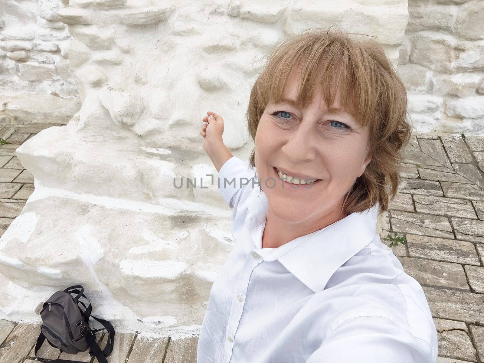 A blonde woman enjoys her adventure by taking a selfie at a historic site, capturing a moment of happiness during her travels.