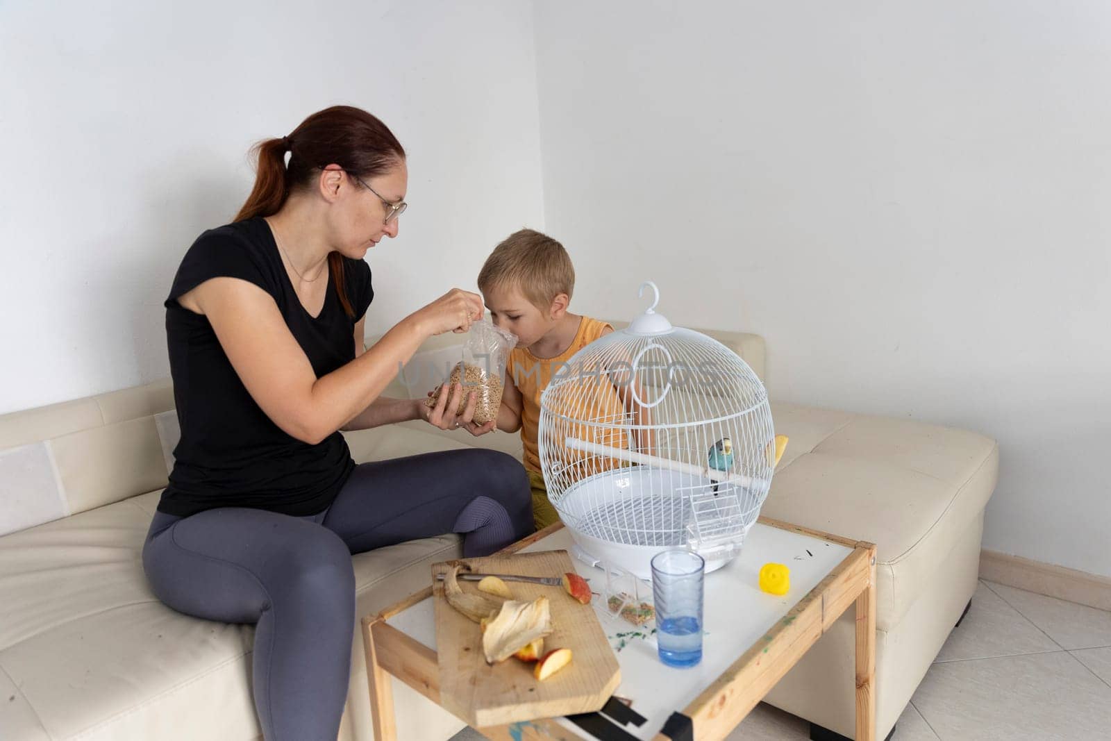 Mother and son preparing food for their pet budgie, promoting responsible pet ownership and family bonding