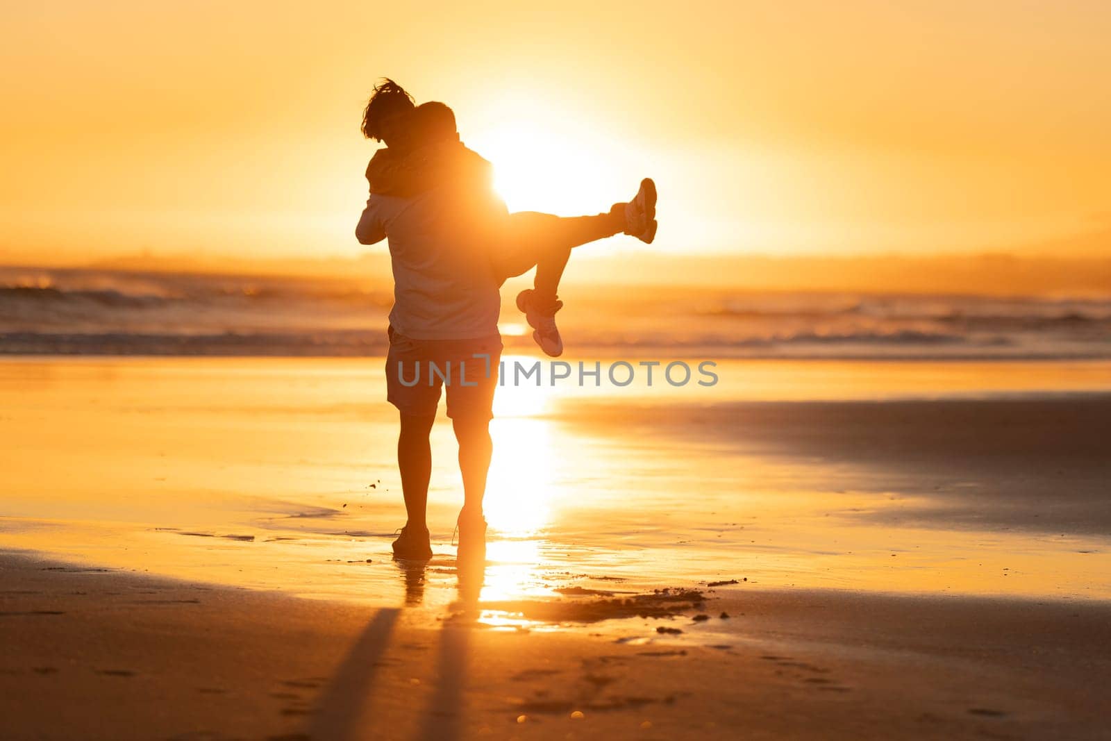 Romantic couple enjoying piggyback ride on beach during golden hour sunset