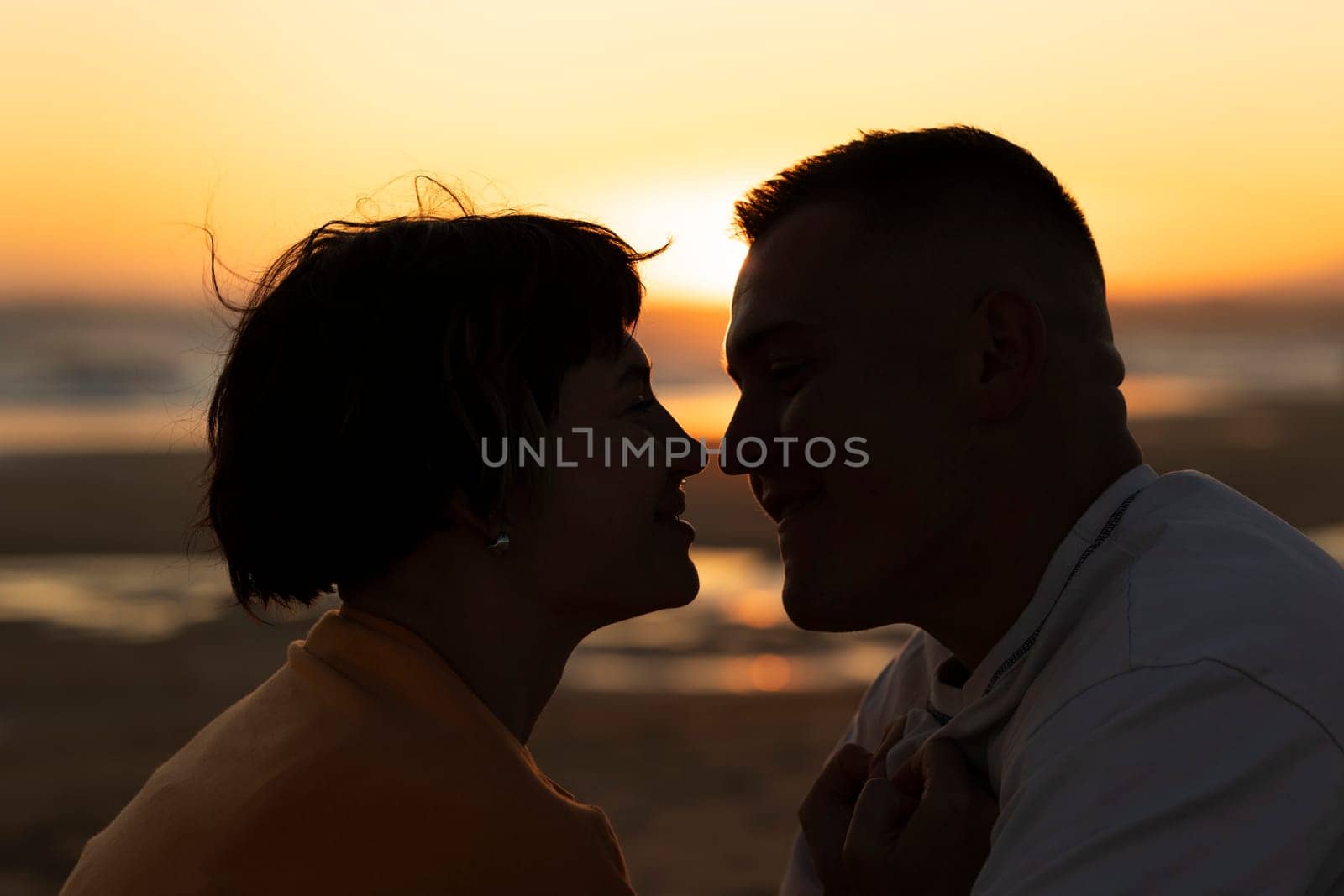 Silhouette of romantic couple touching noses on beach at sunset, enjoying tender moment