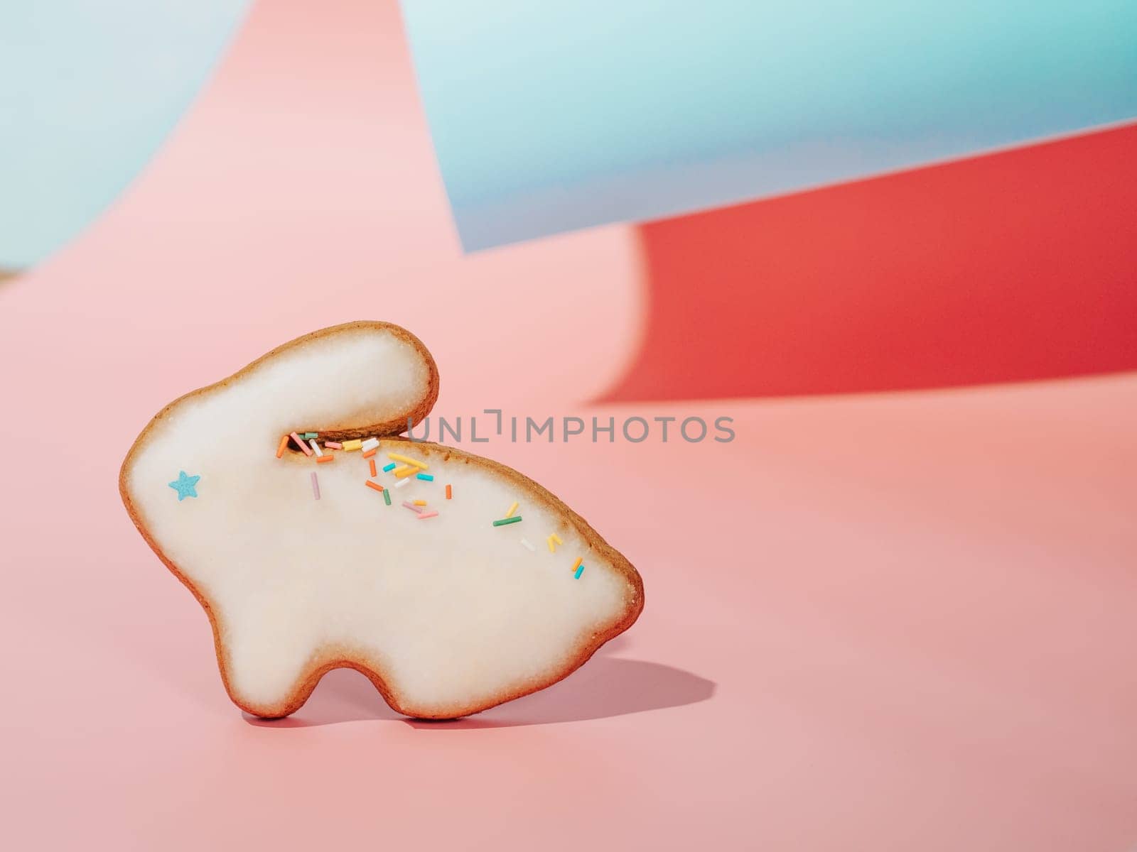 Easter bunny cookie on pink and blue curved paper pastel background with shadows. Happy Easter Day concept. Minimal Easter concept. Copy space. Easter cooking baking background.