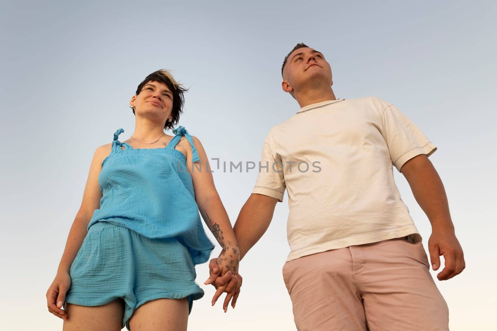 Romantic couple holding hands and looking up at sky, enjoying peaceful moment together