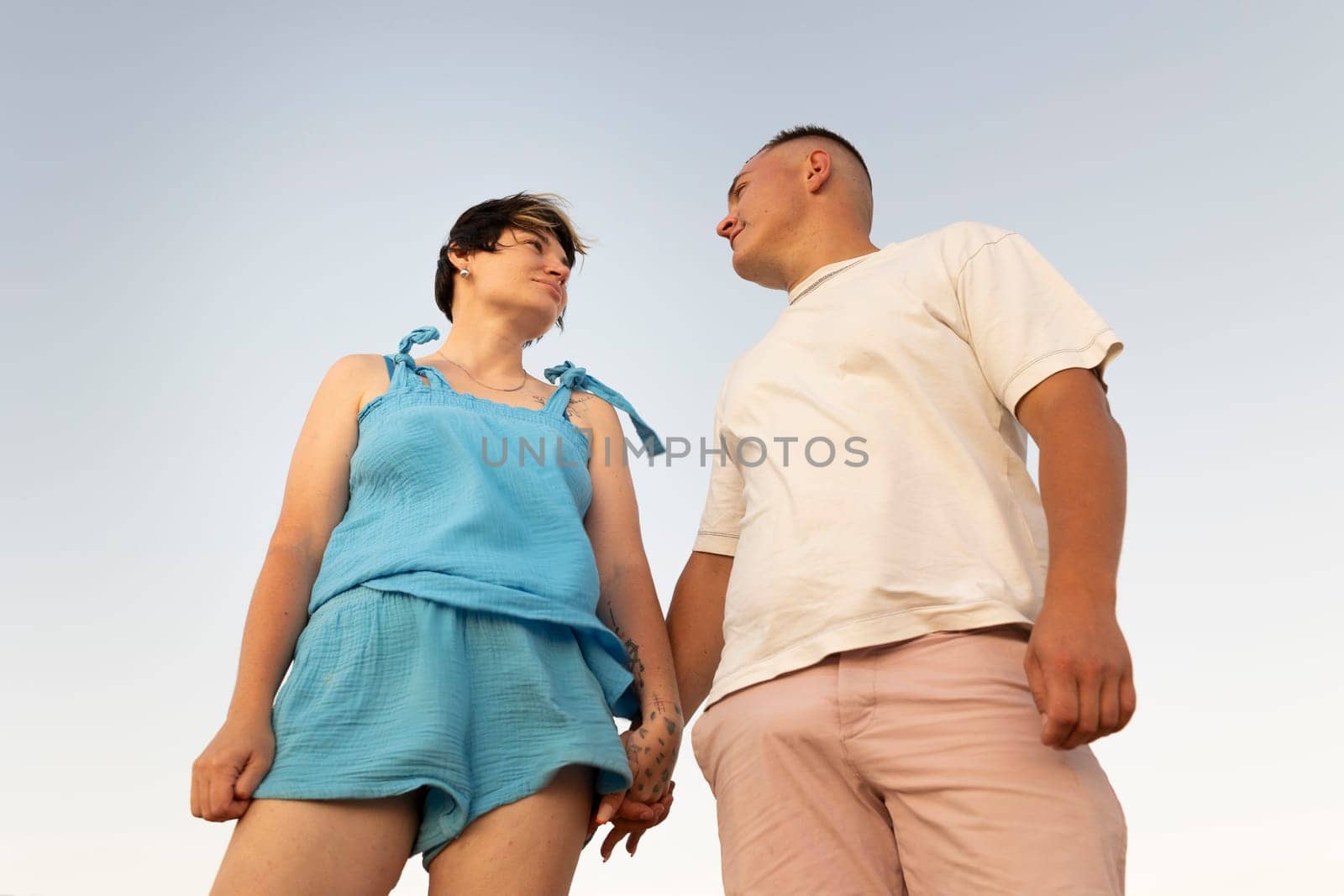 Romantic couple holding hands and looking at each other under a clear blue sky