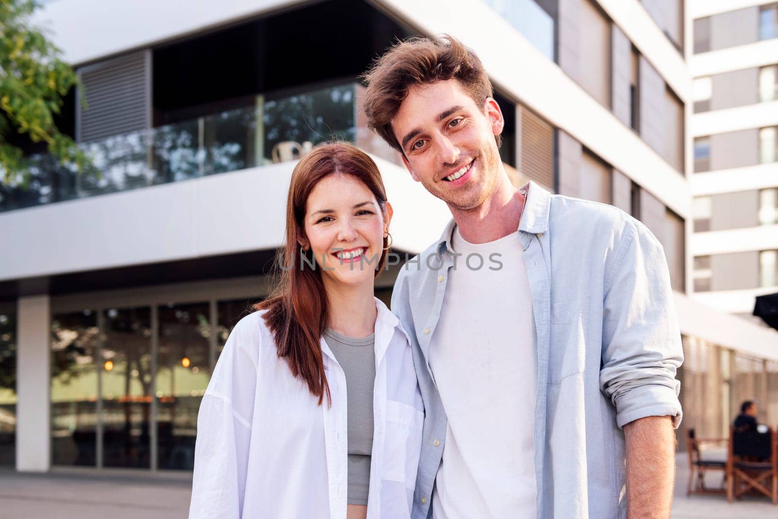 young man and woman smiling happy looking at camera in front of a building, concept of family home and real estate
