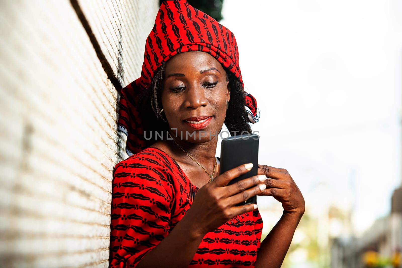beautiful adult woman in red loincloth standing near a wall looking at her mobile phone while smiling.