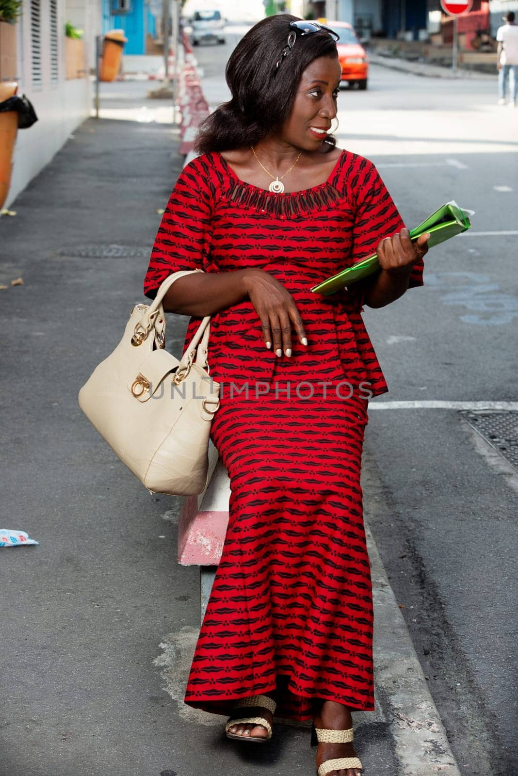 beautiful african adult woman sitting in red loincloth on the street, holding in hand a green document with a beautiful looking sourrie side