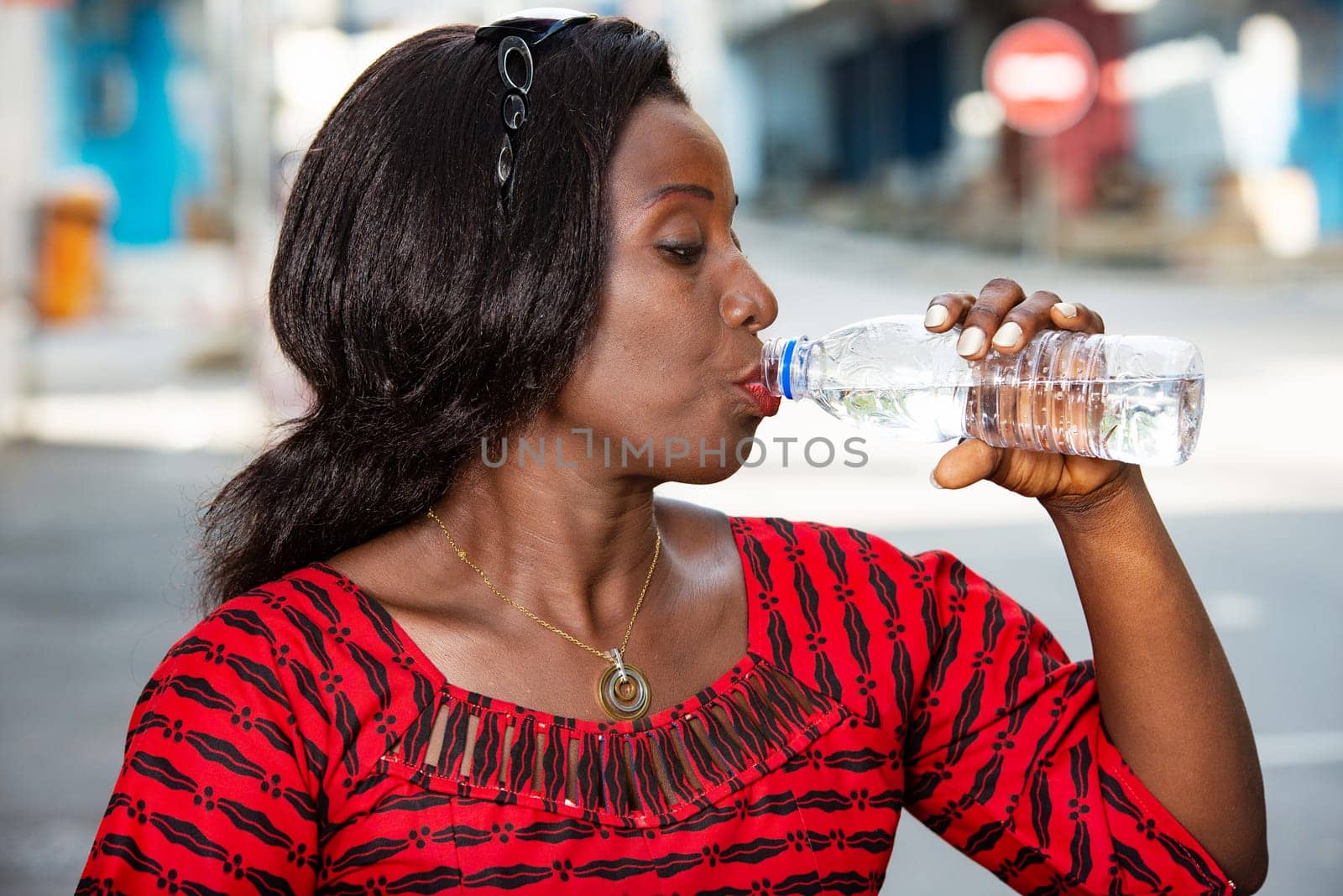 side view, businesswoman in red dress, off desks and drinking bottled water