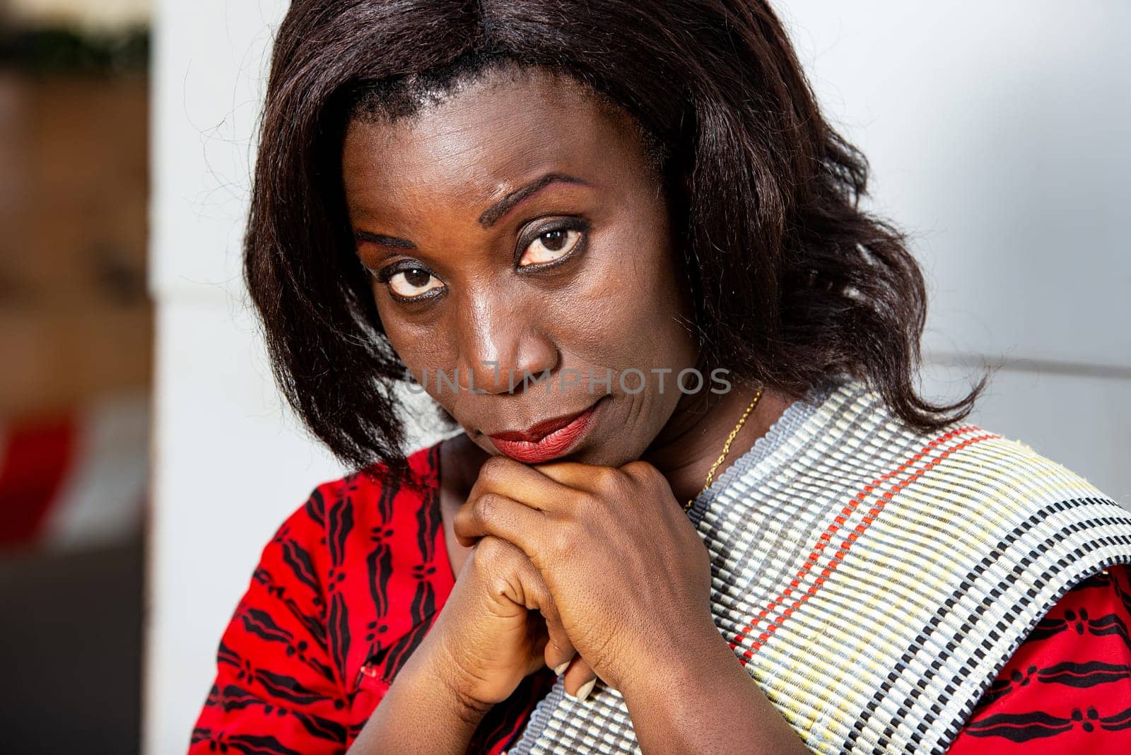 beautiful adult businesswoman dressed in red plaid loincloth sitting holding her hands on her chin while looking in profile.