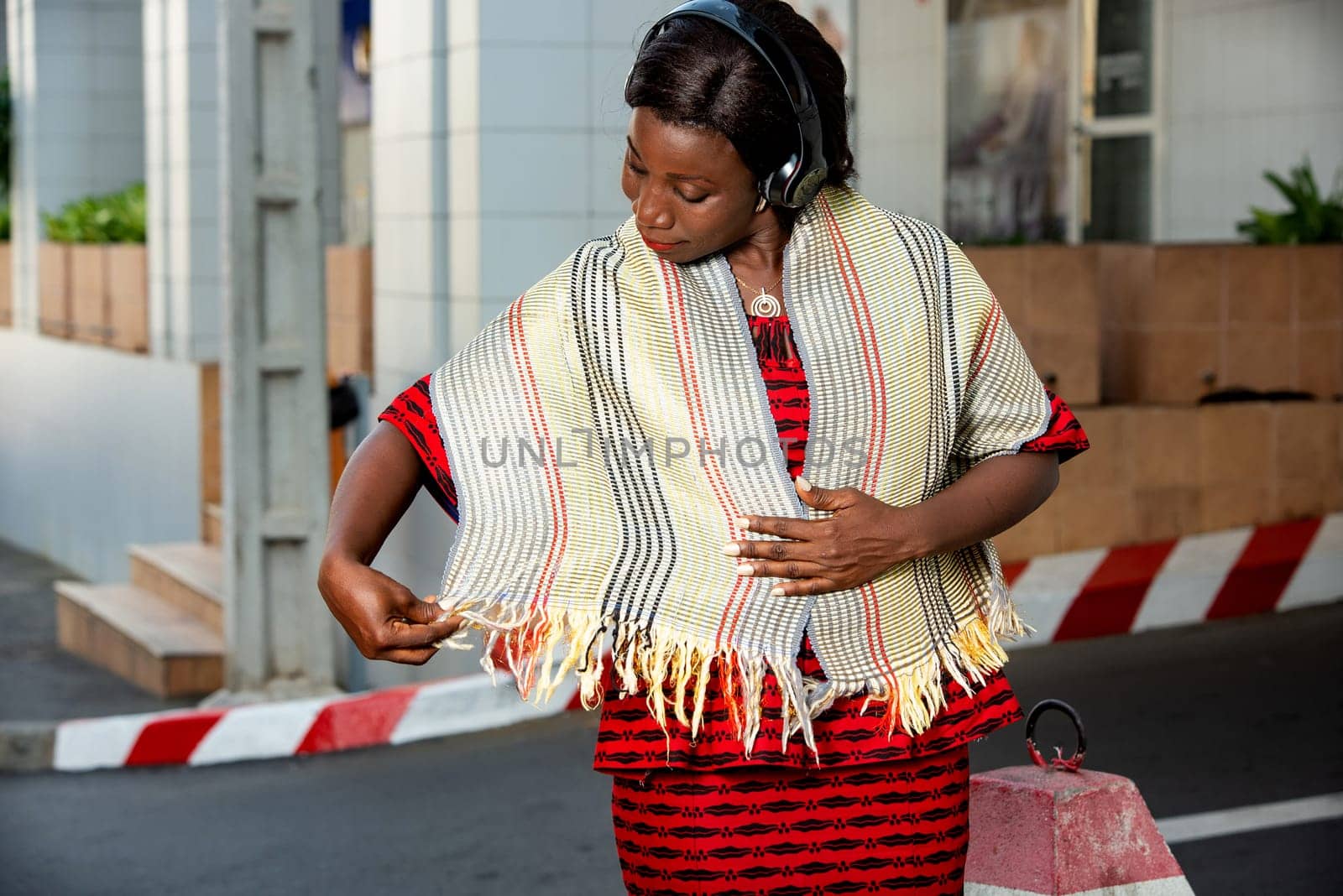 beautiful adult businesswoman dressed in red loincloth, admire her pretty scarf around her neck, in the street while listening to music in her headset