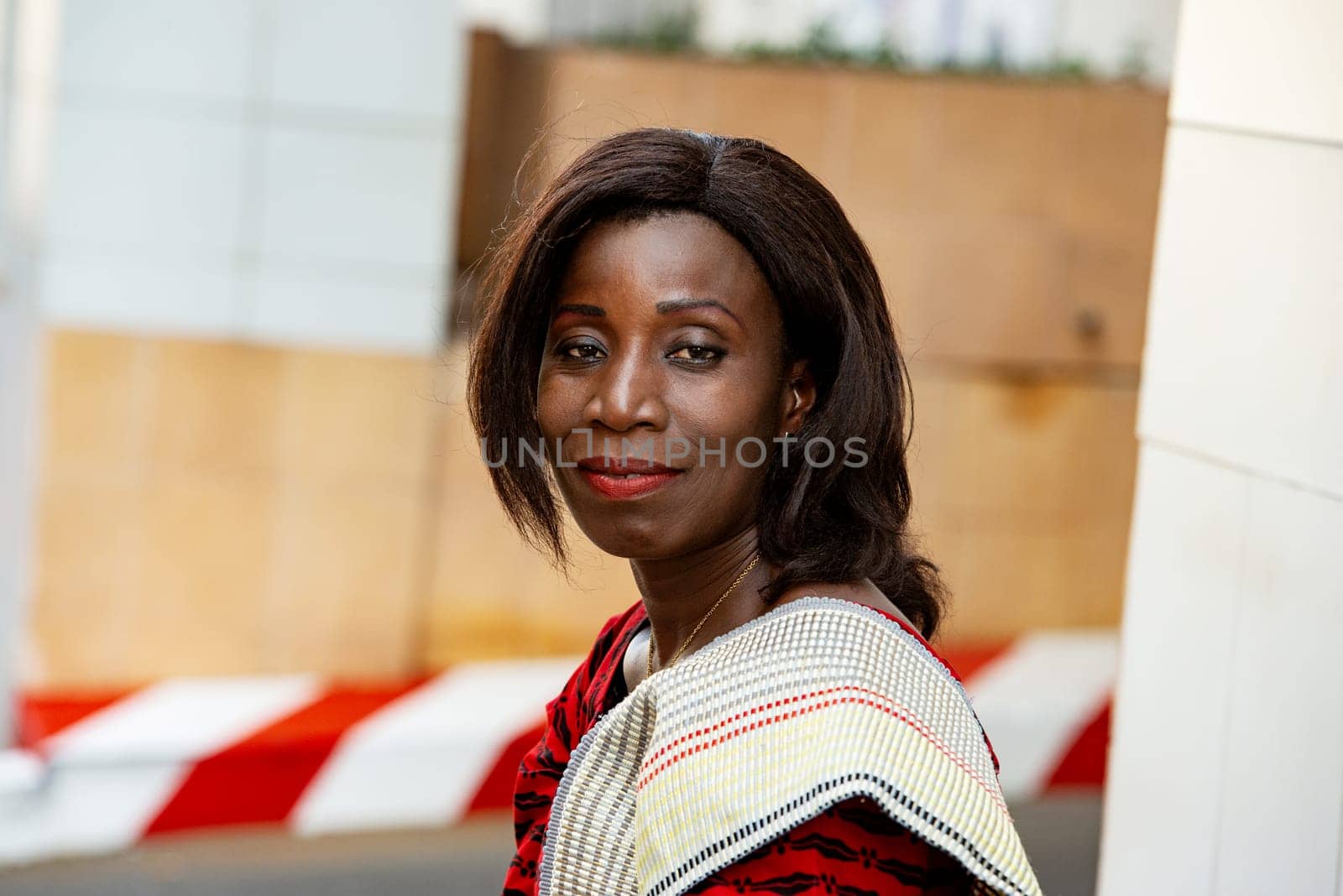 mature african woman in traditional outfit standing outdoors looking at camera smiling.