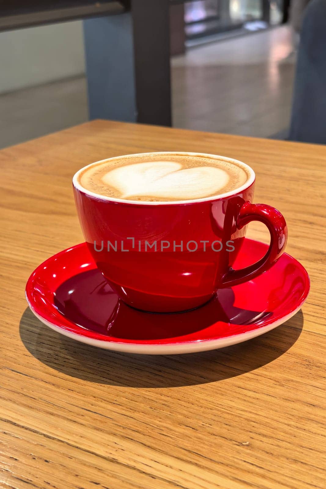 Coffee with heart pattern in bright red cup standing on wooden table in cozy cafe