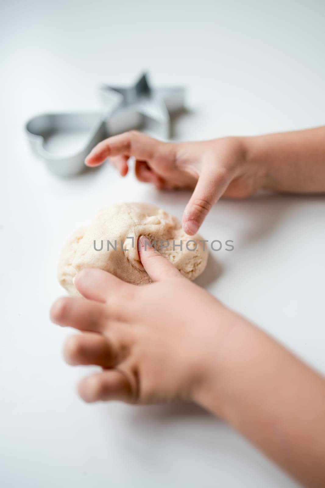 Child playing with dough on white surface.