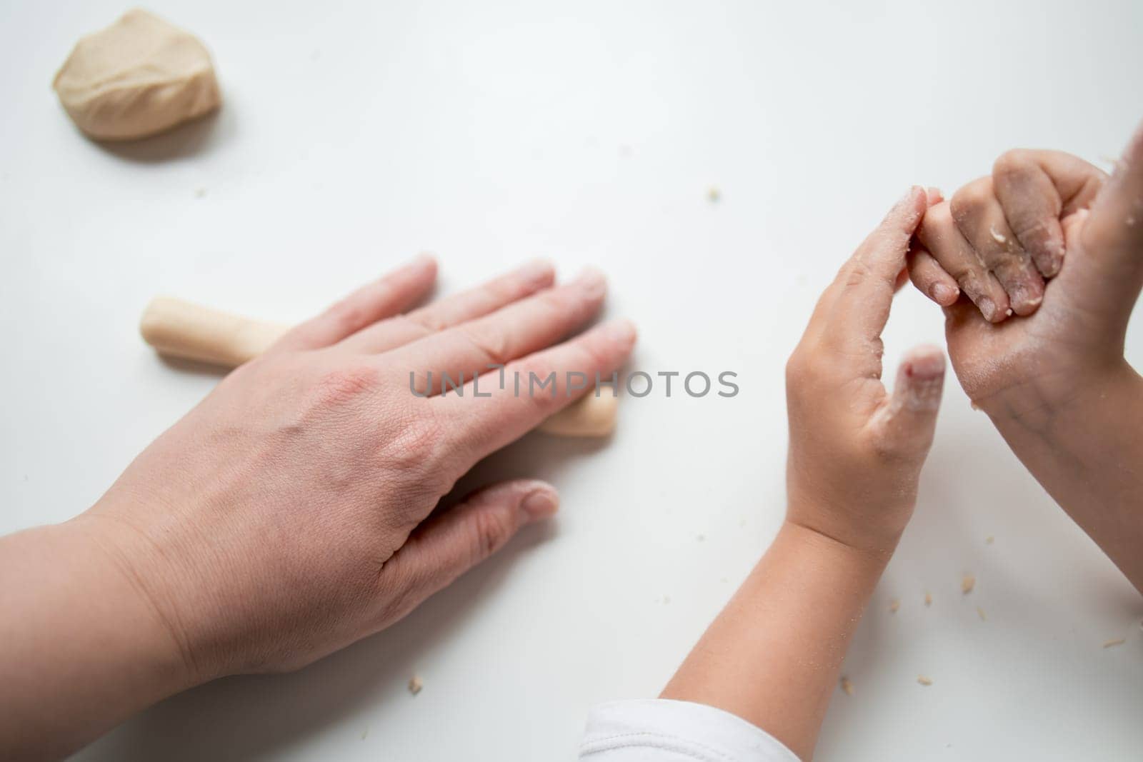 Caucasian adult and child hands working with dough on white surface.