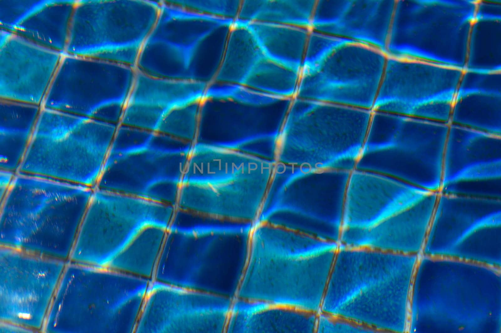 Sunlight glimmers through clear water, creating mesmerizing patterns on the cool blue tiles below, inviting relaxation.
