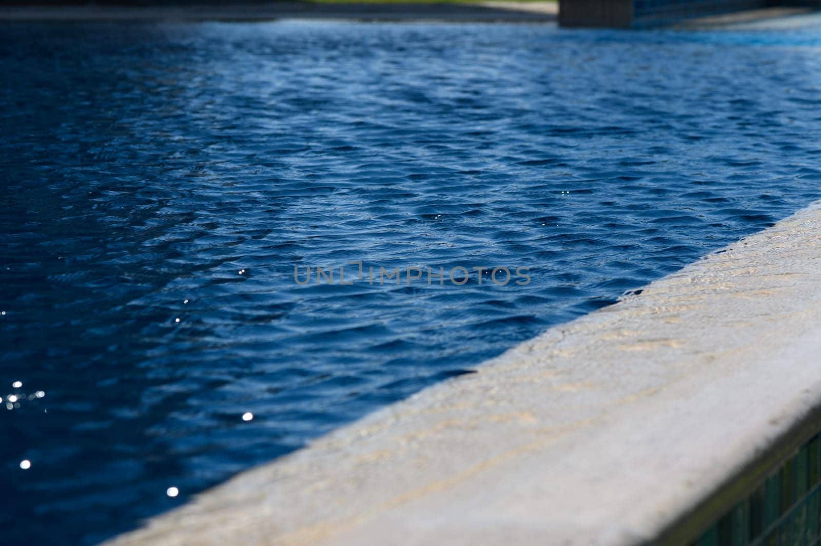 Calm ripples dance on the vibrant water surface, reflecting sunlight at a serene poolside oasis in summer.